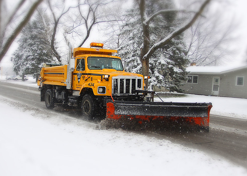 A snow plow truck clears up snow on a residential street