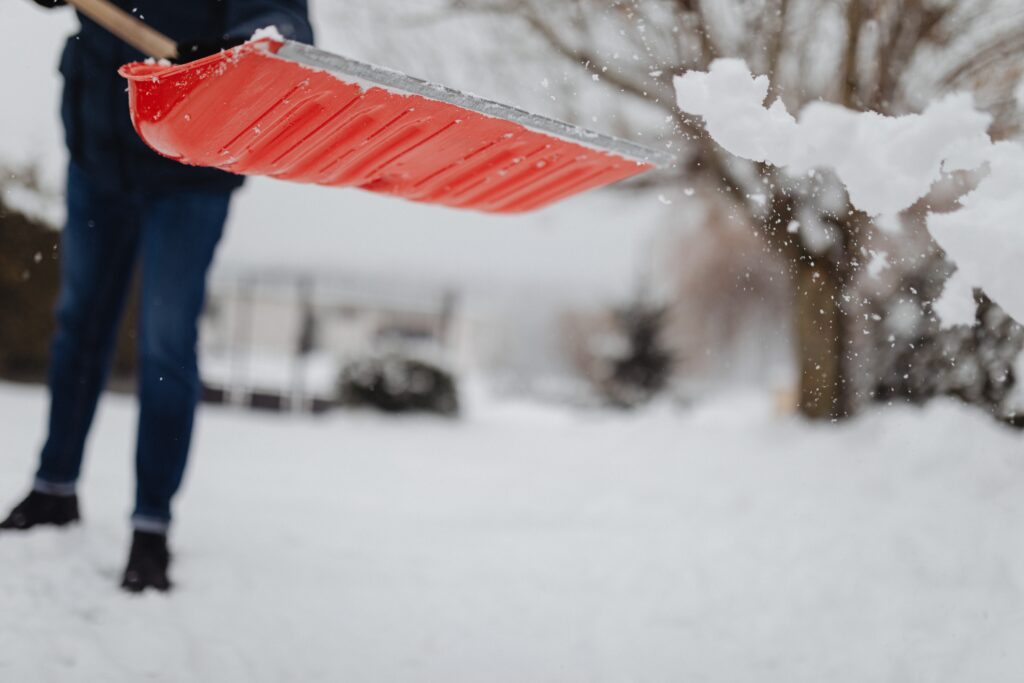 A person flings snow from an orange shovel