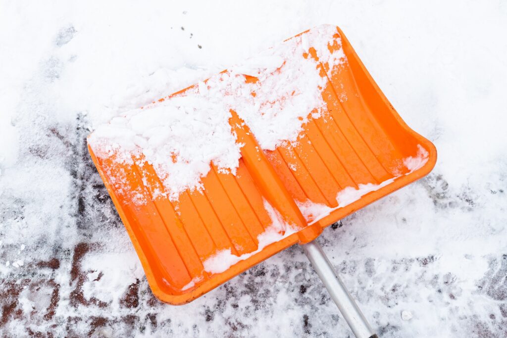 Snow sticks to an orange shovel lying on a brick patio
