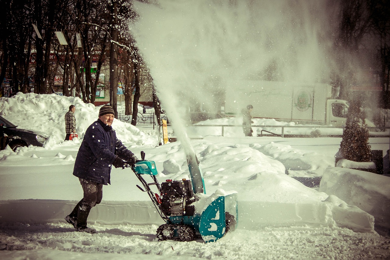 A man using a snow blower to remove the the snow on the streets