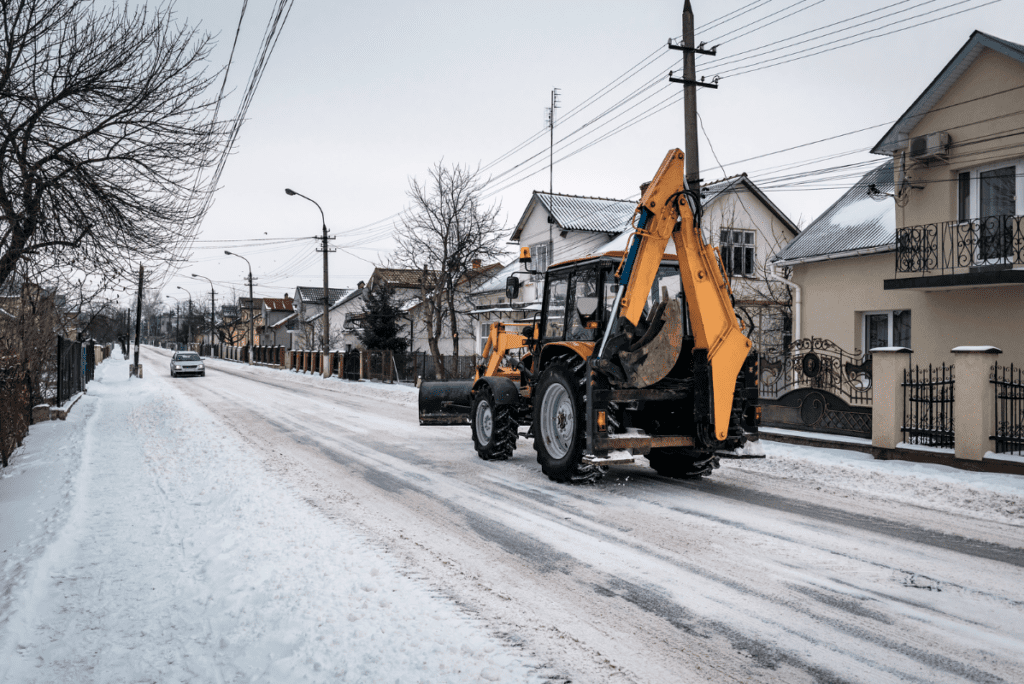 A backhoe drives down a residential street after a recent snow