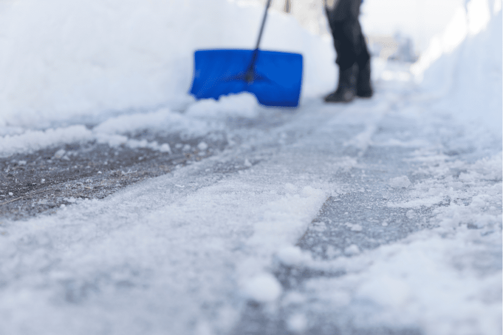 A person clears snow from a walkway with a shovel