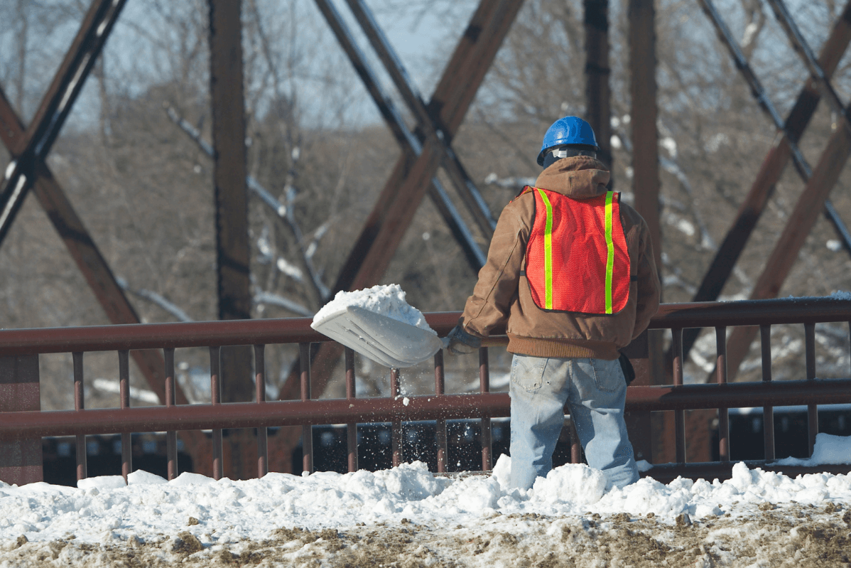 A man shoveling snow off of a bridge