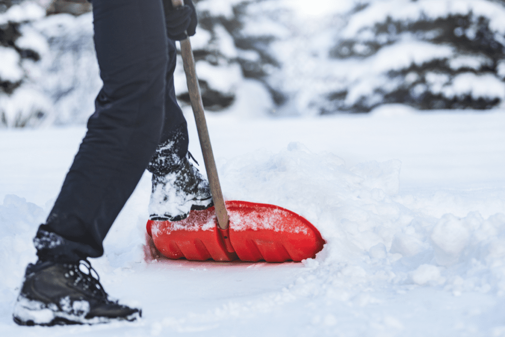 A man pushes a snow shovel with his foot to clear a thick snowfall