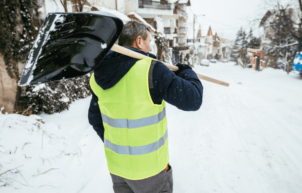 A man with snow shovel cleaning the sidewalks of the street