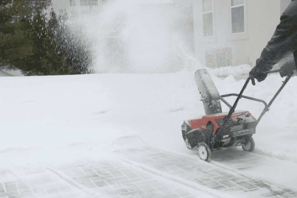 A person clearing a brick driveway with a snow blower