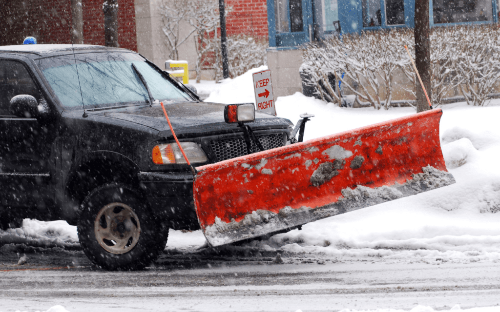 A snow plow truck on a road during a snowstorm