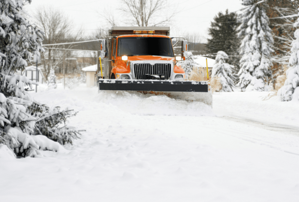 A plow truck plowing thick snow on a village street