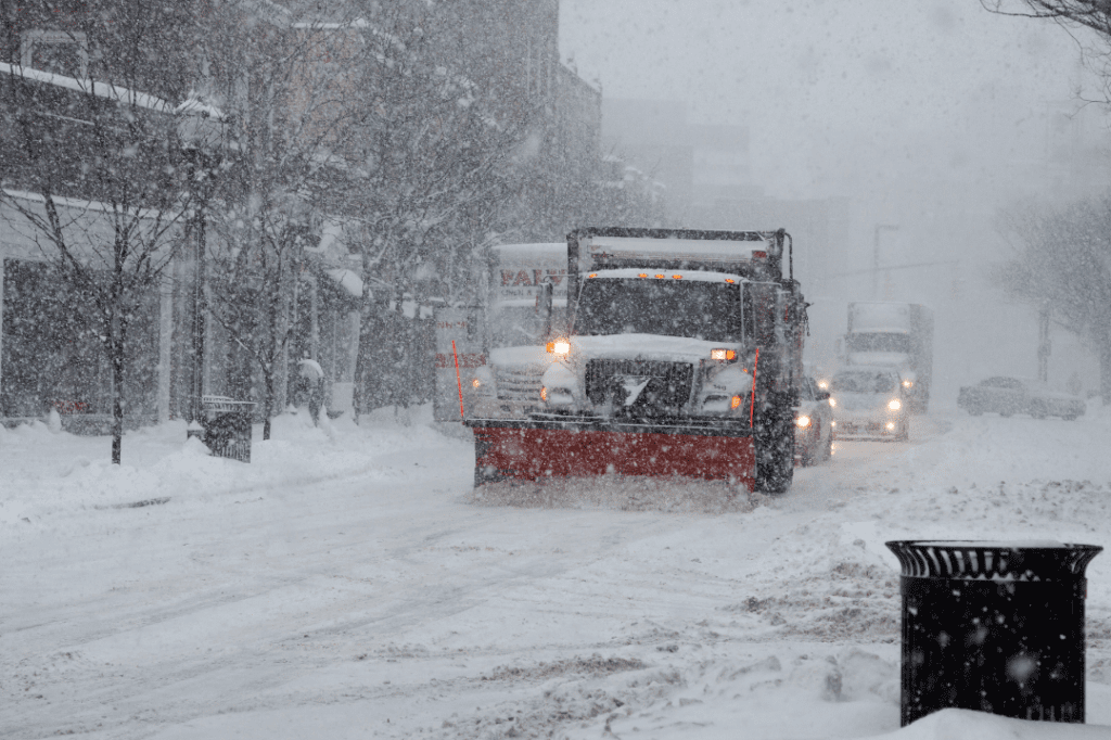 A plow truck driving through the busy streets during a snowstorm to clear out snow