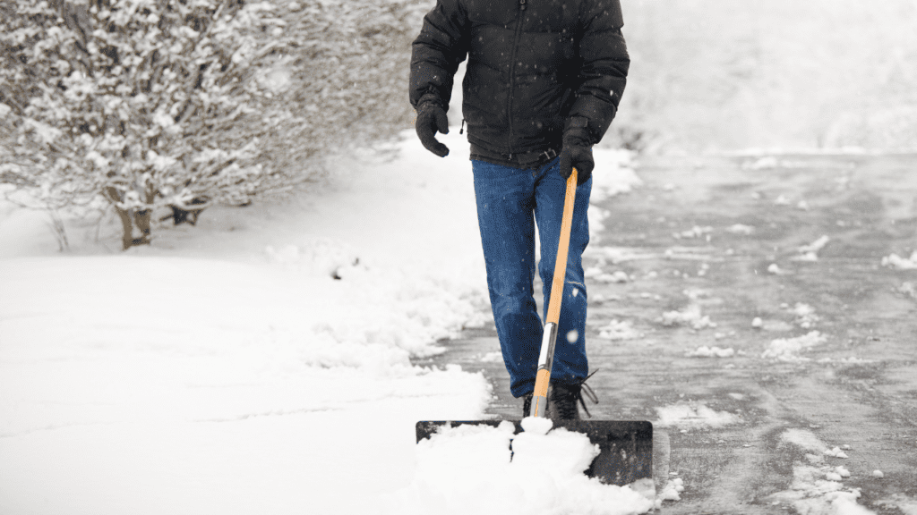 A man scraping snow from the street with a shovel