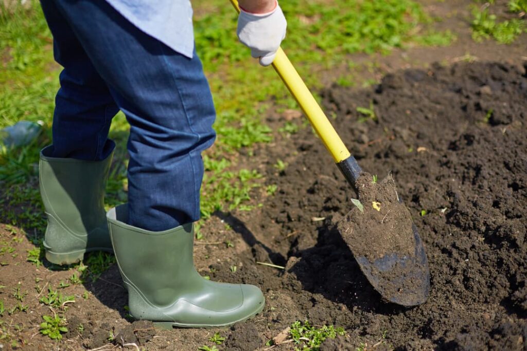 Man with shovel and boots digging in dirt.