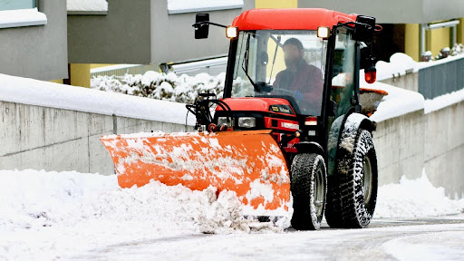 A Person driving a snow plow tractor on an uphill road
