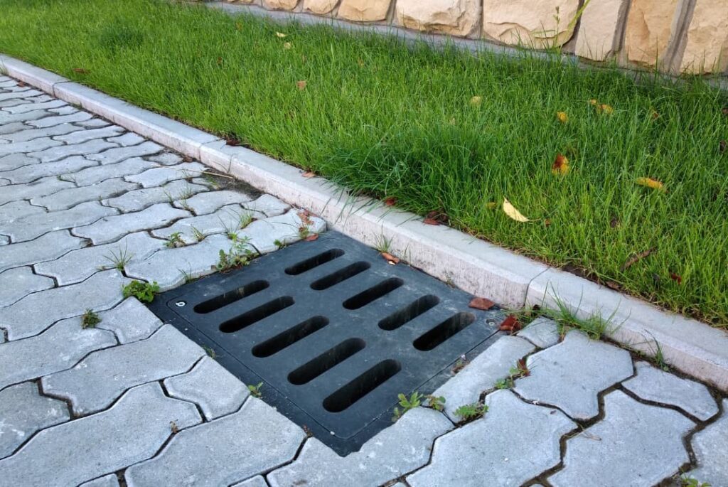 Drain gutter in a green grass lawn and stone pavement sidewalk in Naperville