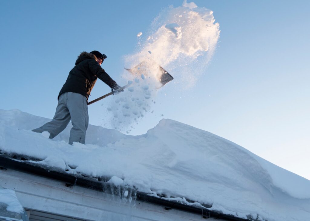 A snow removal expert removing snow from the commercial roof