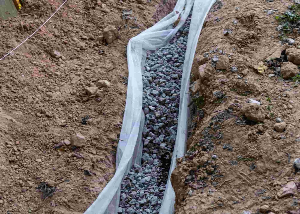 Drainage rock in a French drain as part of a DIY home repair of drainage issues.